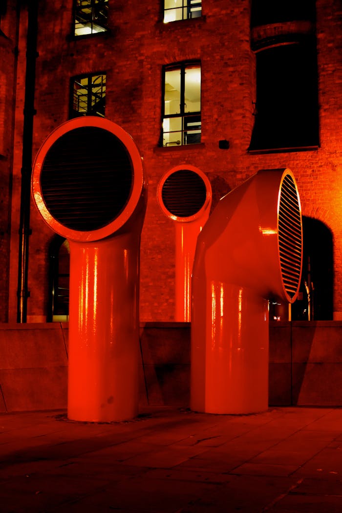 Bold red industrial ventilation pipes in a modern urban landscape at night.